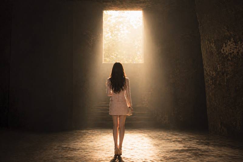 어두운 공간에서 빛을 바라보며 서 있는 여성의 뒷모습, 절망 속에서 희망과 방향을 찾는 순간